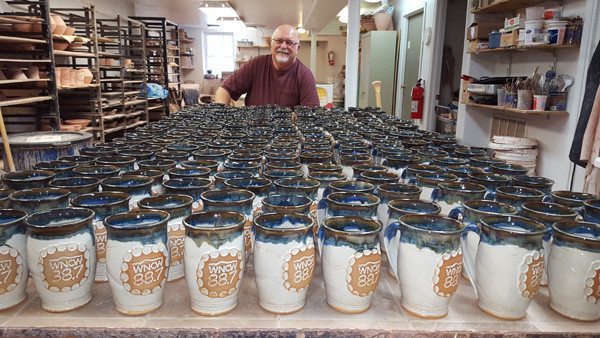 Bob Meier, owner of Doe Ridge Pottery in downtown Boone, stands behind about 200 WNCW mugs. 