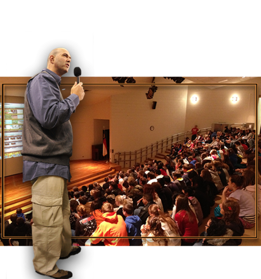 Gabriel standing. In the background is a school assembly. Photo courtesy of Sold Out NC website.